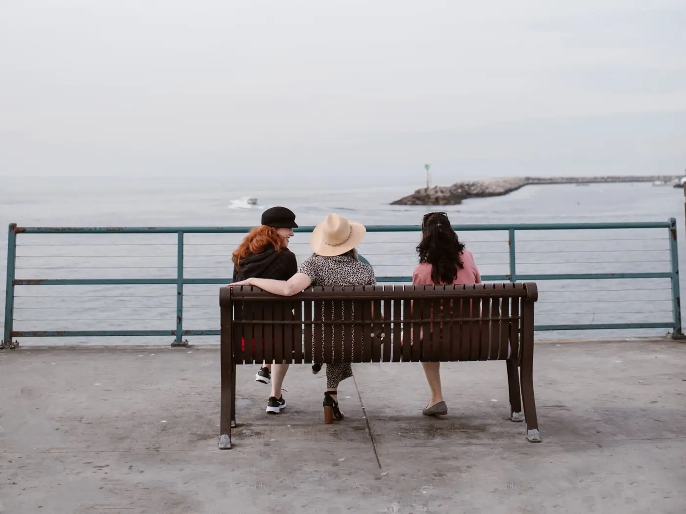 Tres personas conversando sentadas en un banco frente al mar