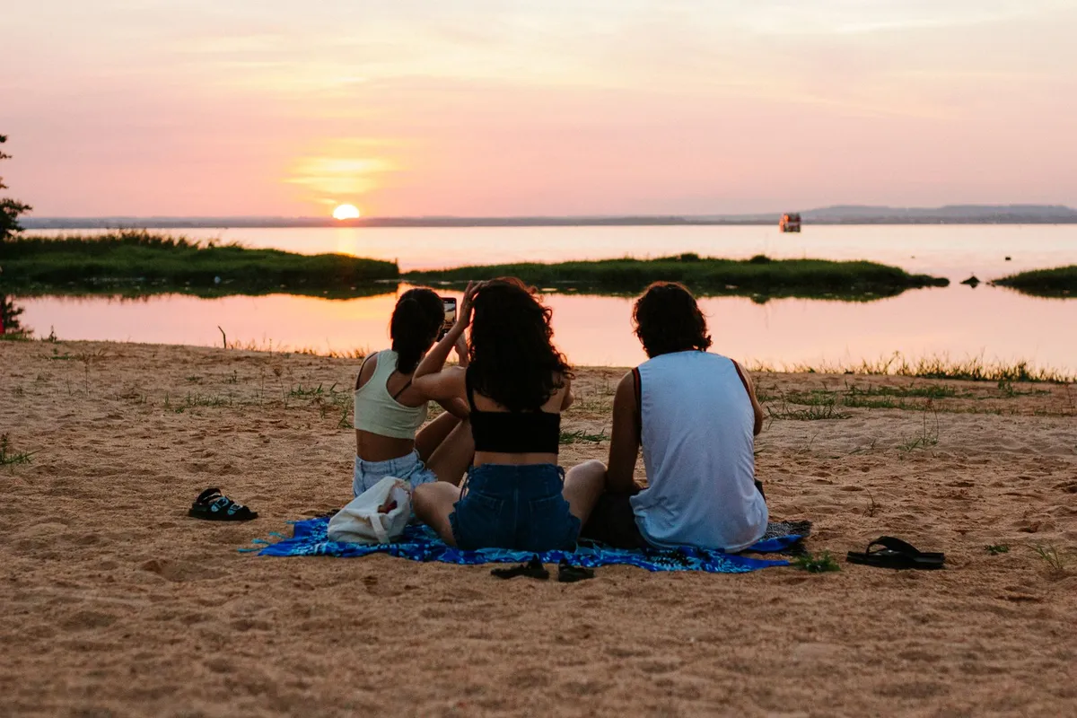 Tres amigos sentados en la playa al atardecer en verano